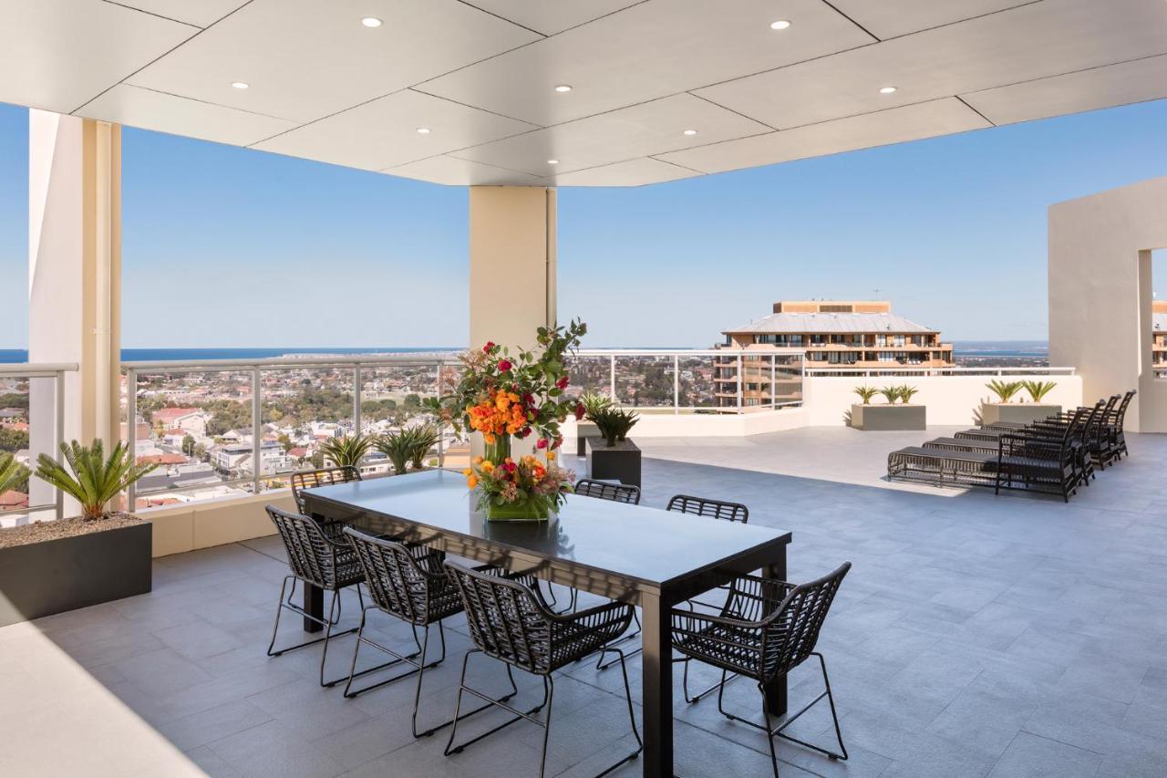 Meriton Suites Bondi Junction Sydney Bagian luar foto The photo shows a stylish outdoor terrace or balcony area, featuring a long dining table surrounded by several black wire chairs. The table has a centerpiece of vibrant flowers. The space is well-lit, with a clear view of the horizon in the backgroun