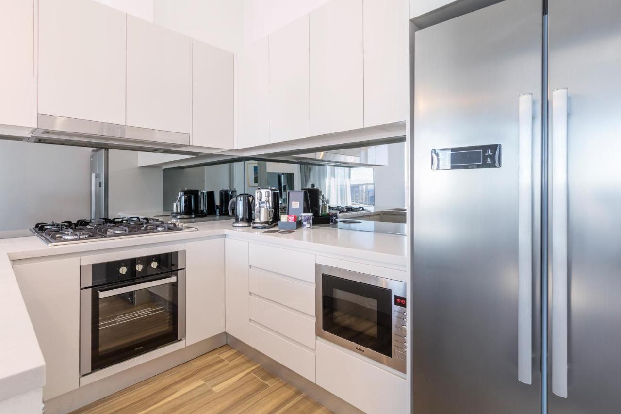 Meriton Suites Bondi Junction Sydney Bagian luar foto The photo shows a modern kitchen with a clean and minimalist design. It features white cabinetry and a stainless steel refrigerator. The kitchen includes a gas stove with an oven below it, as well as a microwave. There are several kitchen appliances,
