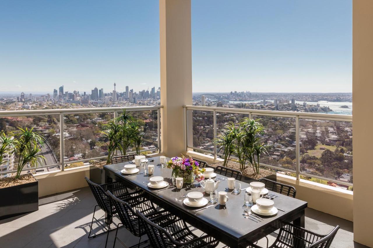 Meriton Suites Bondi Junction Sydney Bagian luar foto The photo shows a beautifully arranged outdoor dining area on a balcony. There is a long black dining table set for a meal, with plates, glasses, and decorative items like a vase of flowers. Surrounding the table are stylish black chairs. In the back