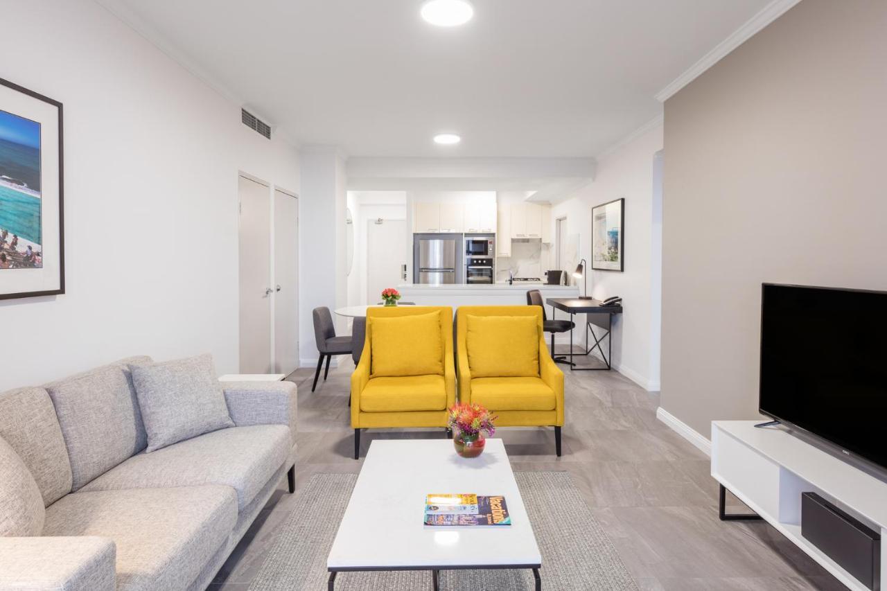 Meriton Suites Bondi Junction Sydney Bagian luar foto The photo shows a modern living space with a light and airy design. In the foreground, there are two bright yellow armchairs flanking a white coffee table, which has a small vase of flowers and a magazine on it. To the left, there is a light gray sof
