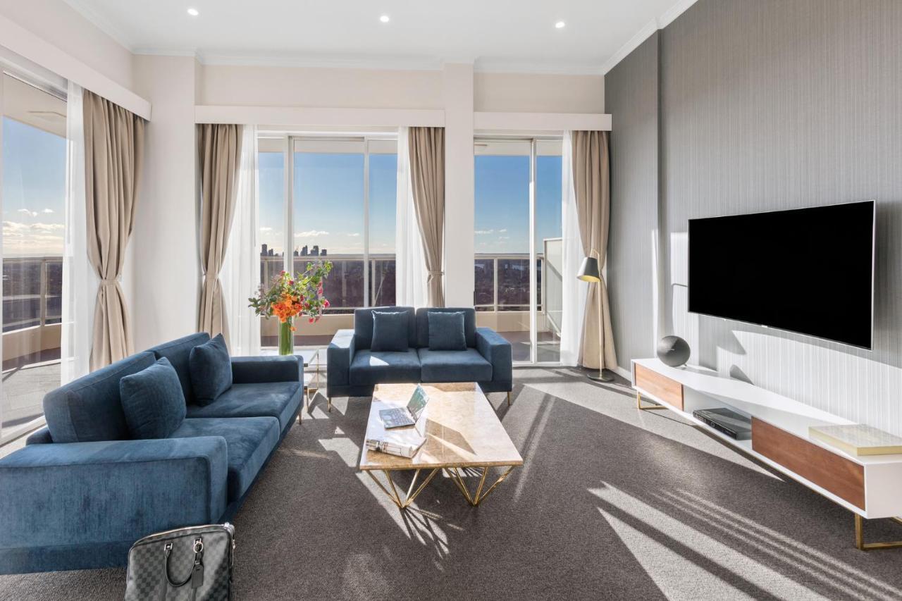 Meriton Suites Bondi Junction Sydney Bagian luar foto The photo depicts a modern living room with a stylish and contemporary design. It features a cozy seating arrangement with a blue sofa and two matching armchairs. In front of the seating area is a coffee table with a geometric design. The room has la