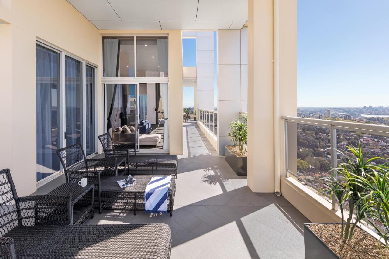 Meriton Suites Bondi Junction Sydney Bagian luar foto The photo shows a spacious balcony or terrace area of a high-rise building. It features modern outdoor furniture, including a seating arrangement with dark wicker chairs and a table. There are cushions, and a blue and white striped blanket is draped 