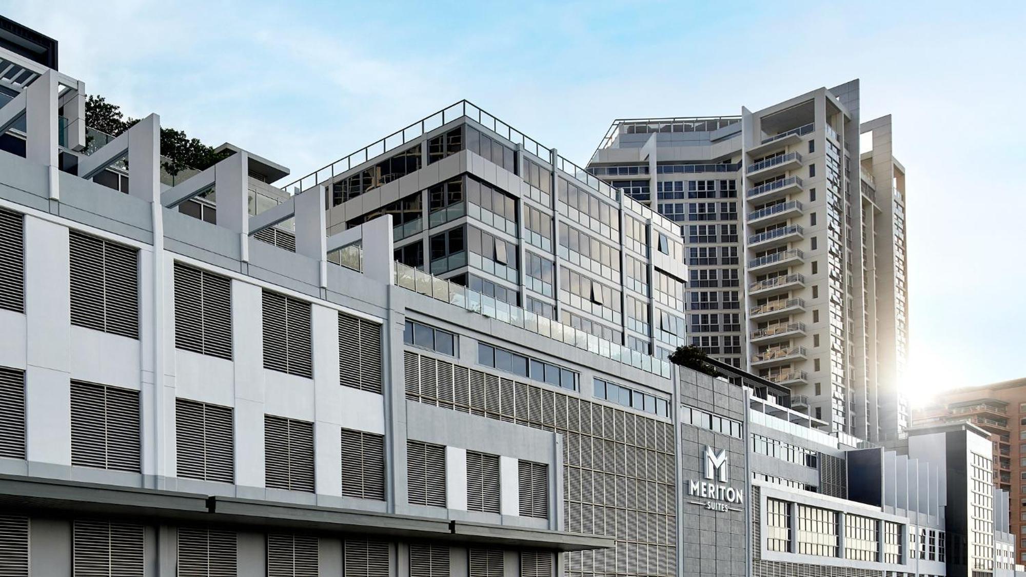 Meriton Suites Bondi Junction Sydney Bagian luar foto The image shows a modern urban building or complex. The structure features a combination of glass and concrete elements, showcasing contemporary architectural design. The foreground has a lower section that appears to be a podium or base with a textu